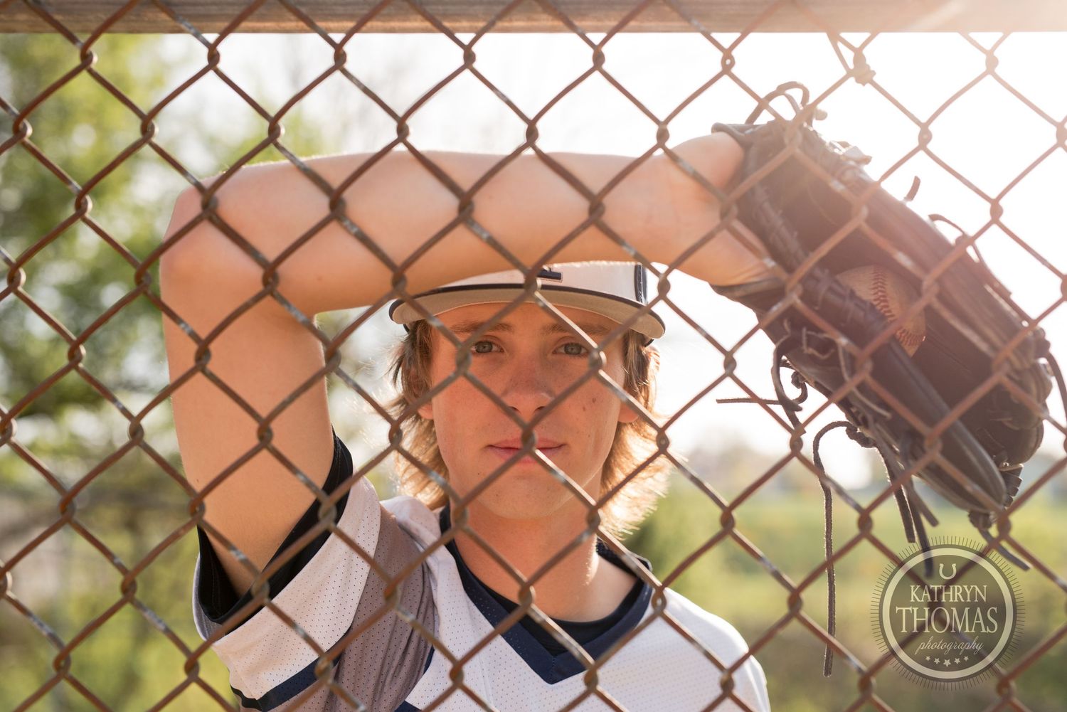 Baseball player with glove peers through chain link fence on baseball field.