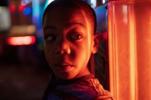 black child is lit up by red lights of an arcade game