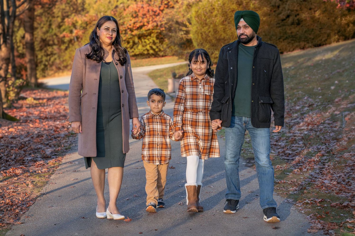 A family takes a walk together on a leaf-covered path during autumn.