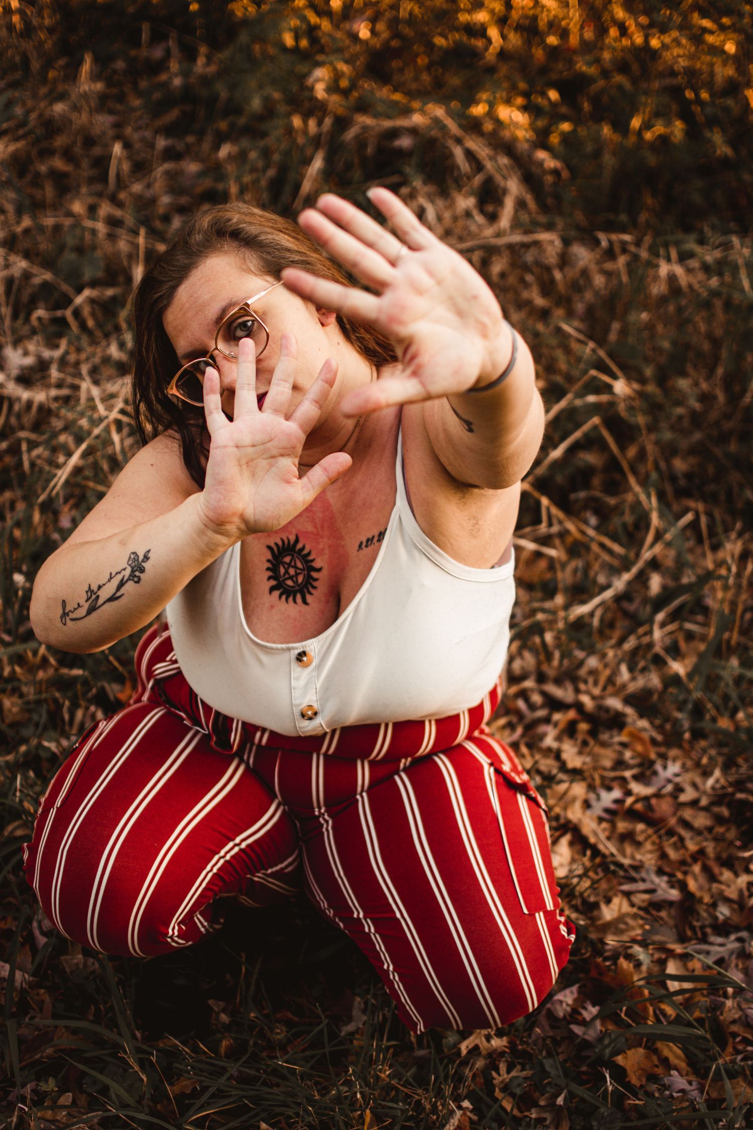 Person in striped pants making playful hand gestures while sitting in fallen autumn leaves.