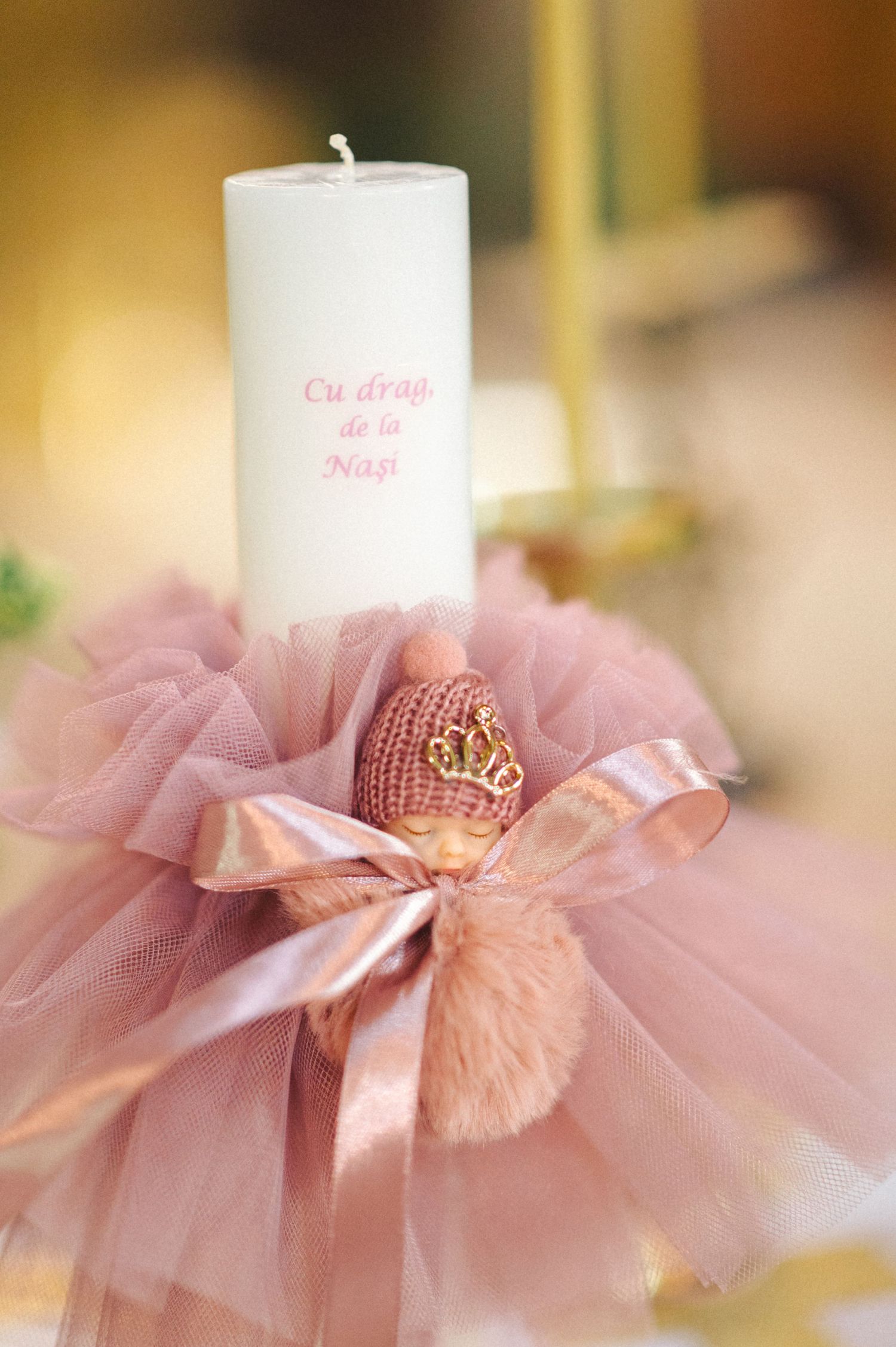 Decorative white candle with pink tulle and crown embellishments in soft lighting.