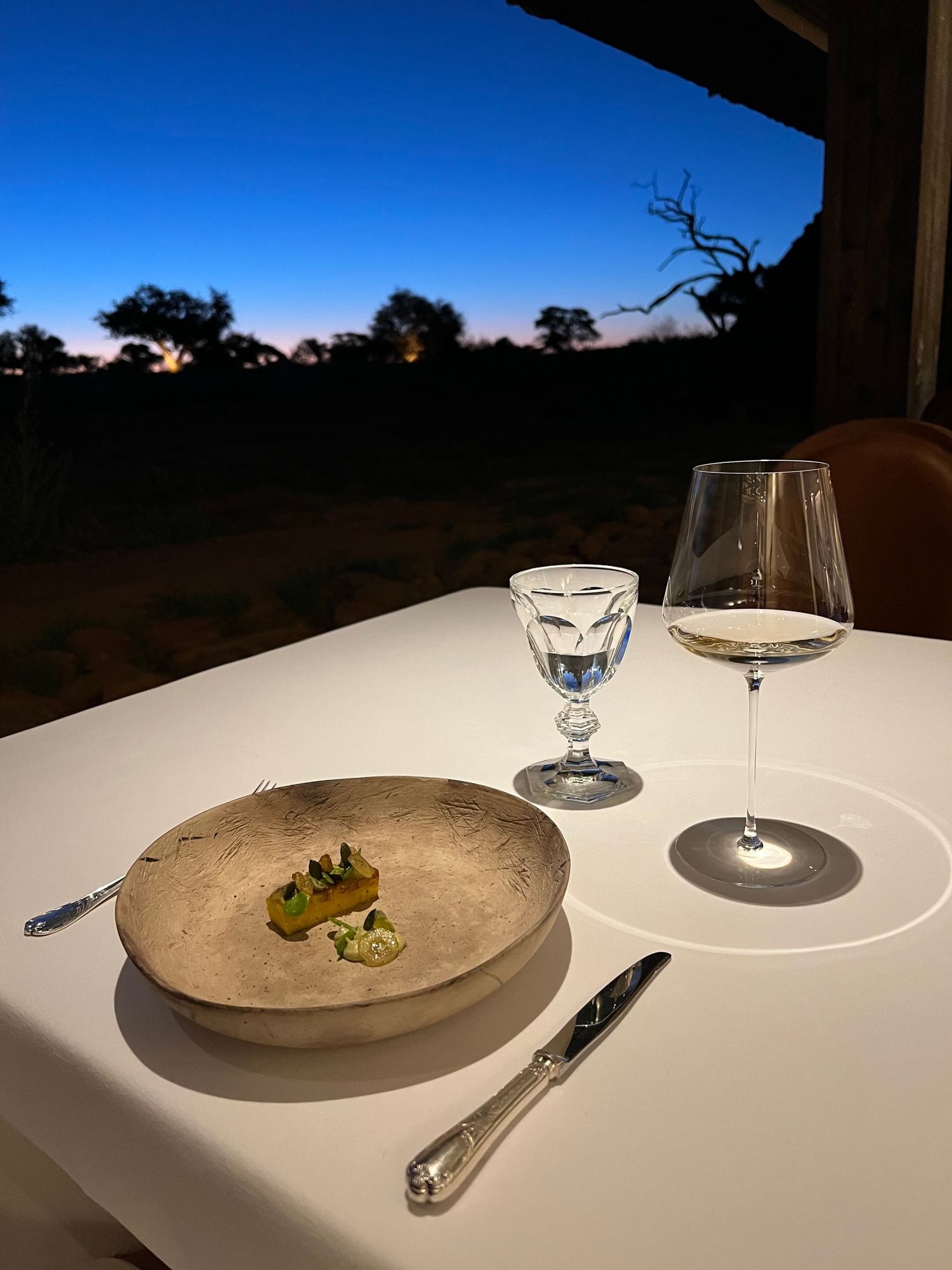 Fine dining table setting at dusk with elegant plates and wine glasses.