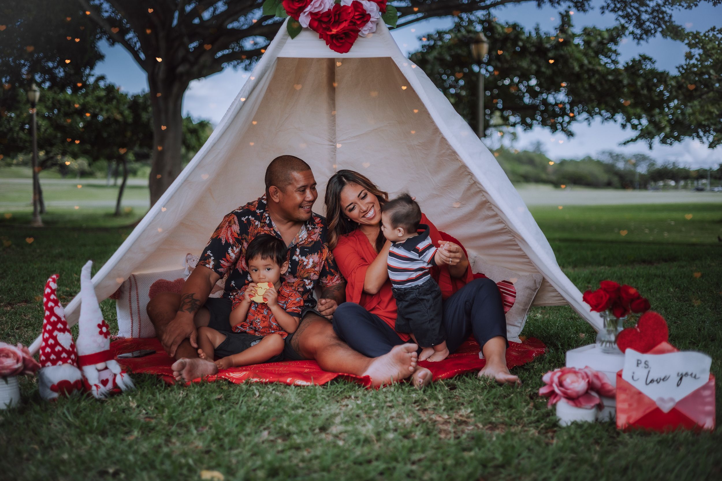 Family relaxing together in white tent with red decorations outdoors.