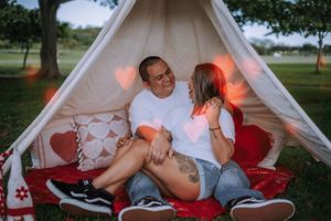Couple sharing tender moments inside a decorated white teepee tent with red accents.