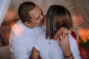 Romantic couple embracing near a white teepee tent during an outdoor photoshoot.
