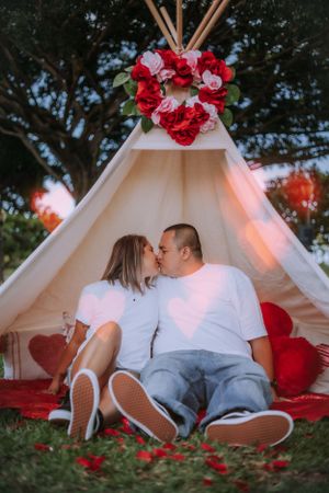 Romantic outdoor photoshoot featuring a white teepee tent adorned with red flowers in a park setting.