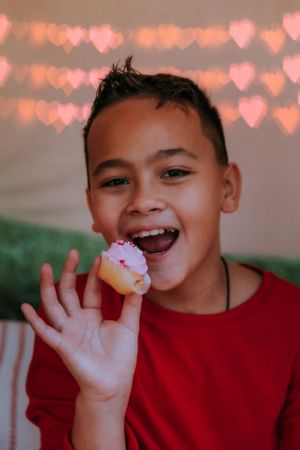 Child in red sweater enjoying snacks with heart-shaped bokeh lights in background.