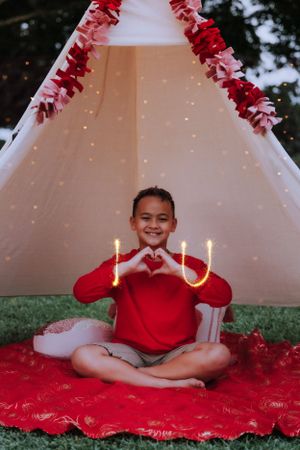White teepee tent decorated with fairy lights and red accents for a magical outdoor setting.