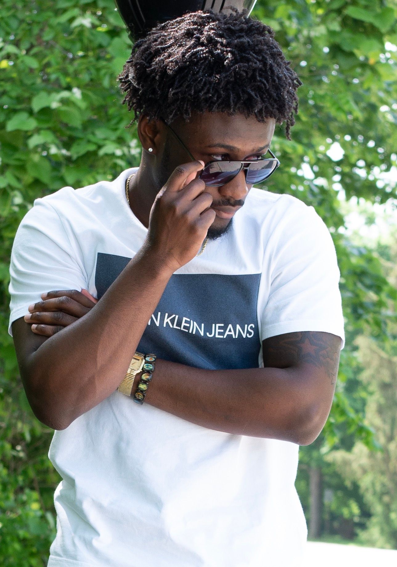 Fashion model in Calvin Klein shirt and sunglasses poses in garden setting.