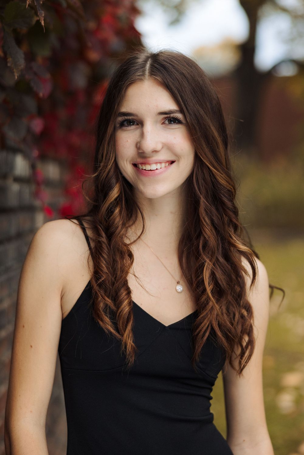 Portrait of someone in a black dress against autumn foliage with red leaves.