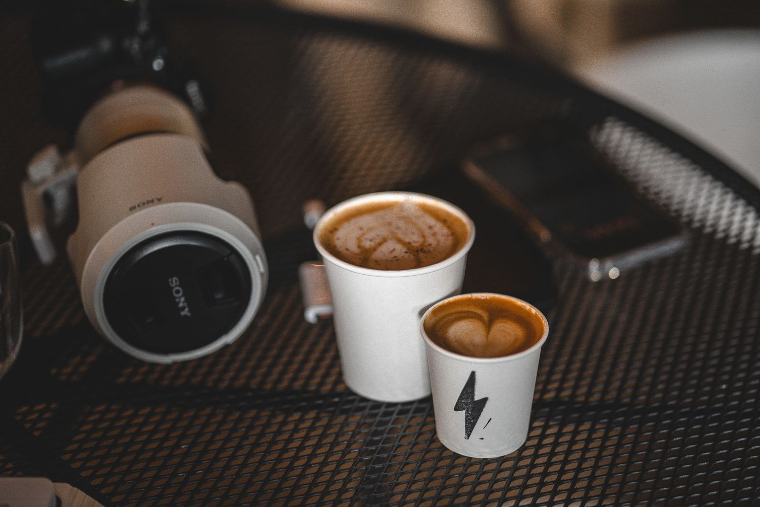 Two small cups of latte art with heart designs displayed on a dark textured surface.