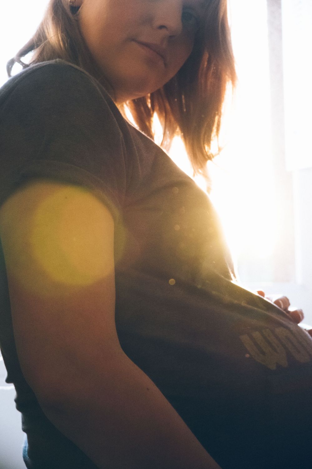 Silhouette of pregnant person against window with lens flare effect.