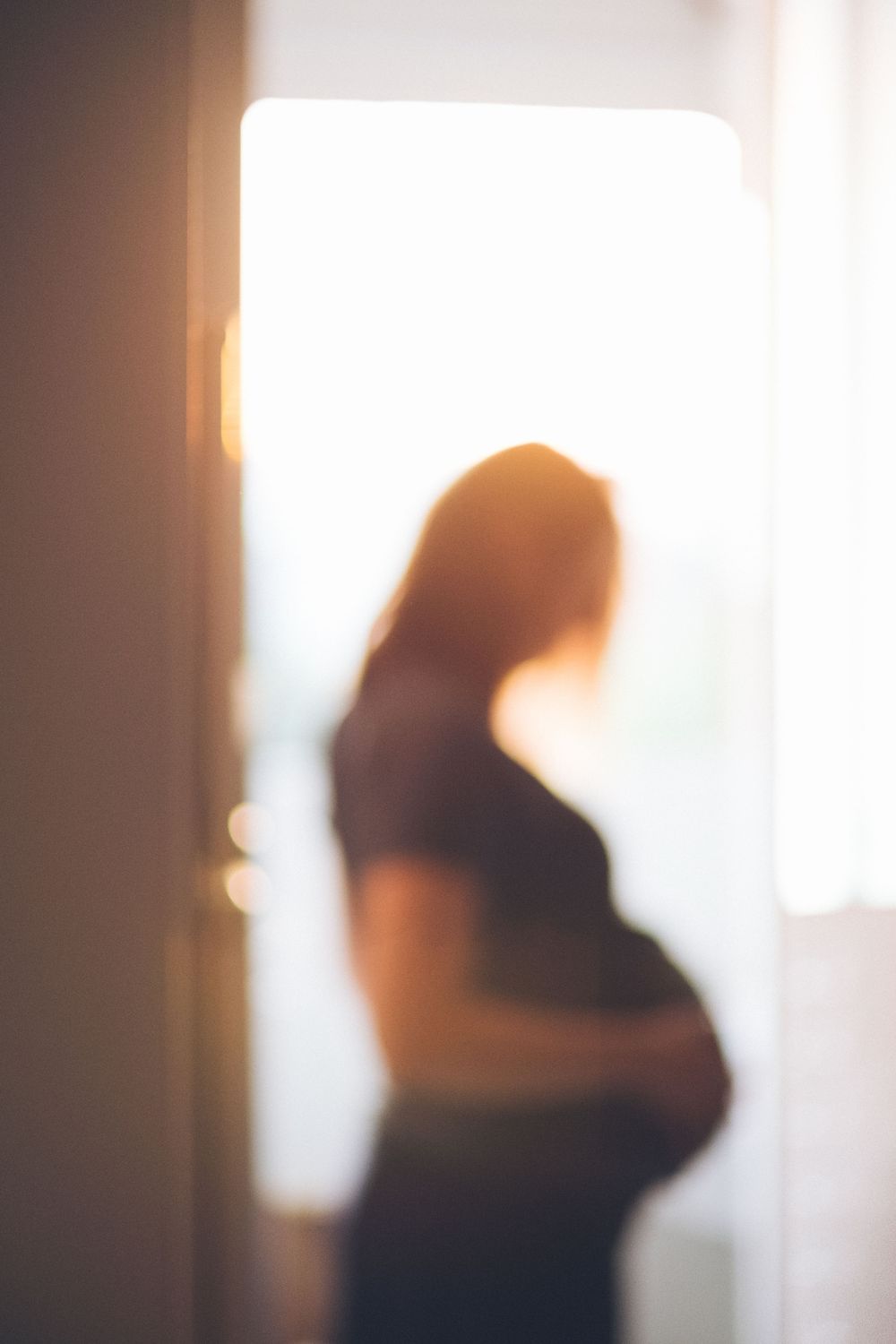 Out of focus silhouette showing pregnant figure against bright window.