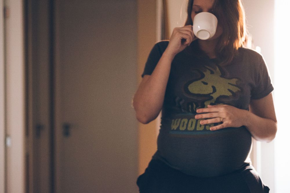 Person wearing graphic t-shirt holds white coffee cup while standing in doorway.