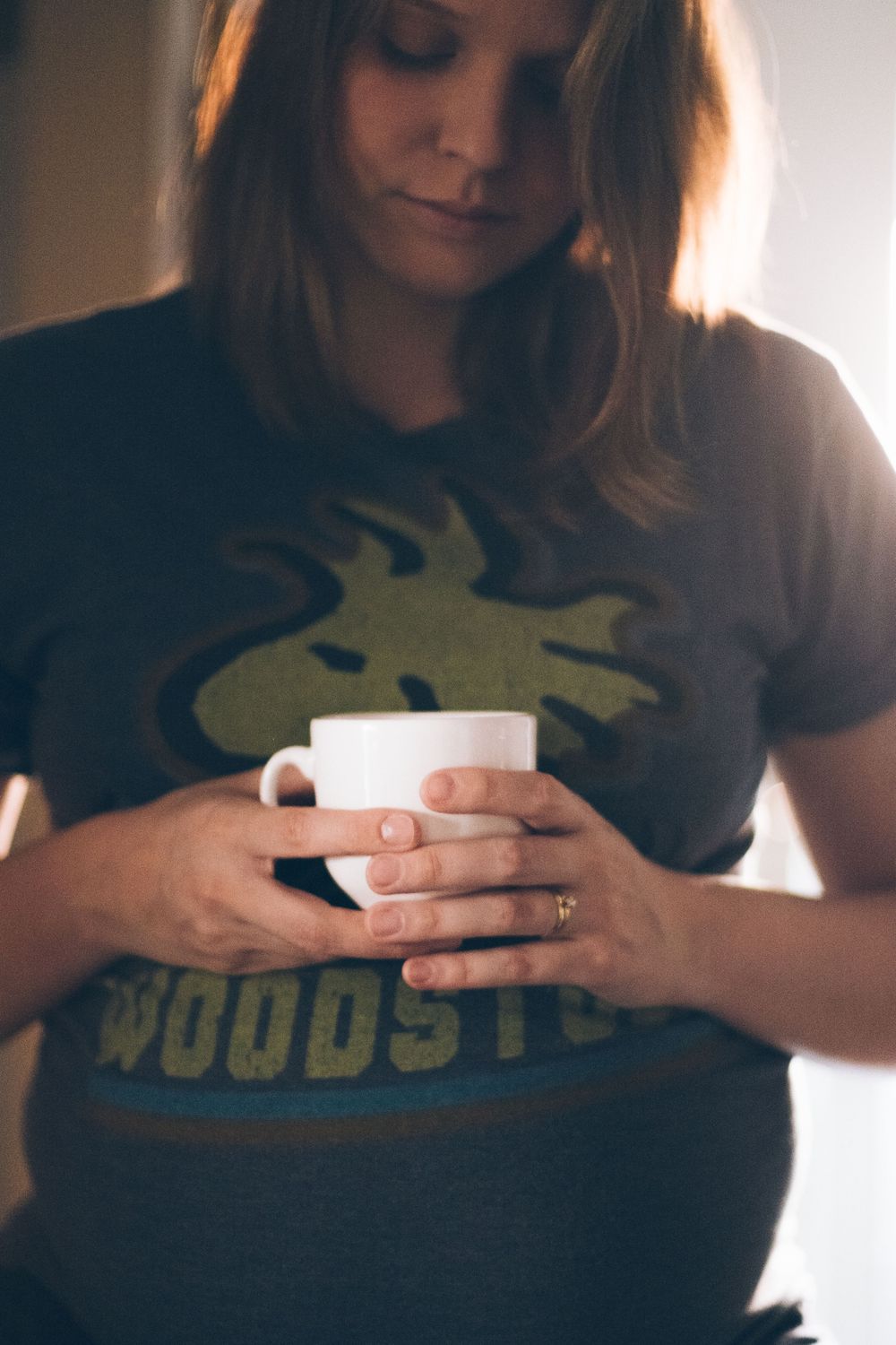 Close-up of hands holding white coffee cup while wearing graphic t-shirt.