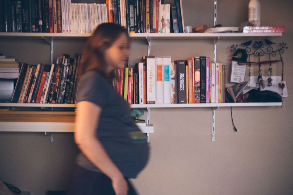 Blurred motion shot of pregnant person walking past bookshelf.