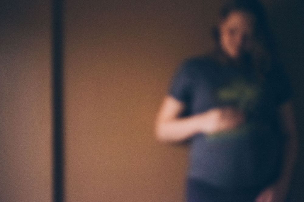 Soft focus image of person in dark clothing standing against warm-toned wall.