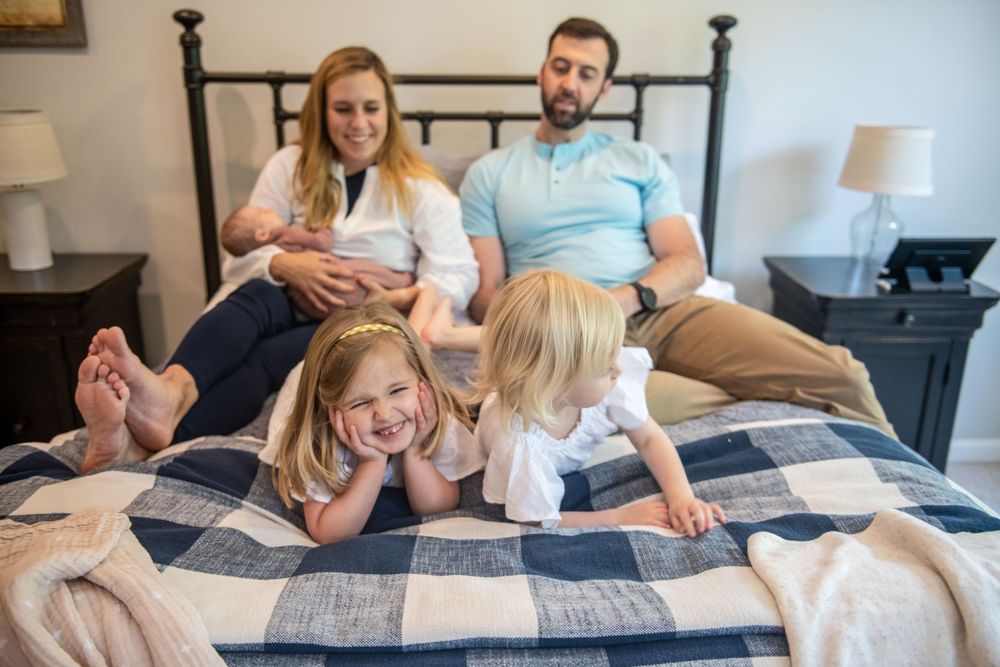 Family relaxing together on a plaid bedspread with young children and an infant.