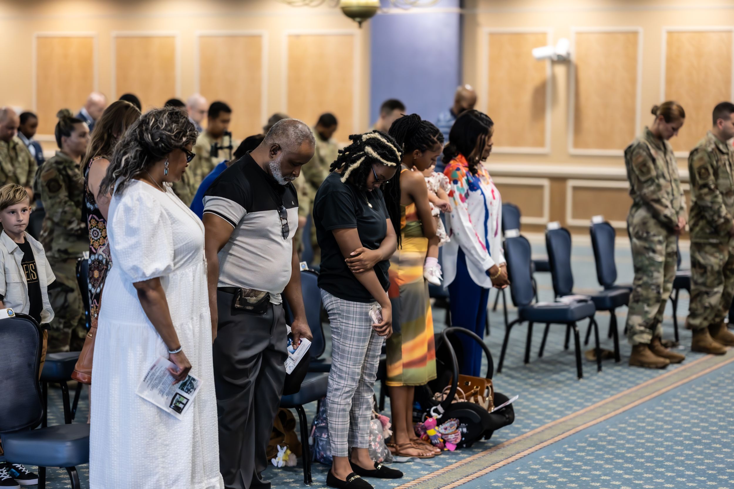 Military personnel and guests gather for a formal ceremony in a carpeted conference hall.