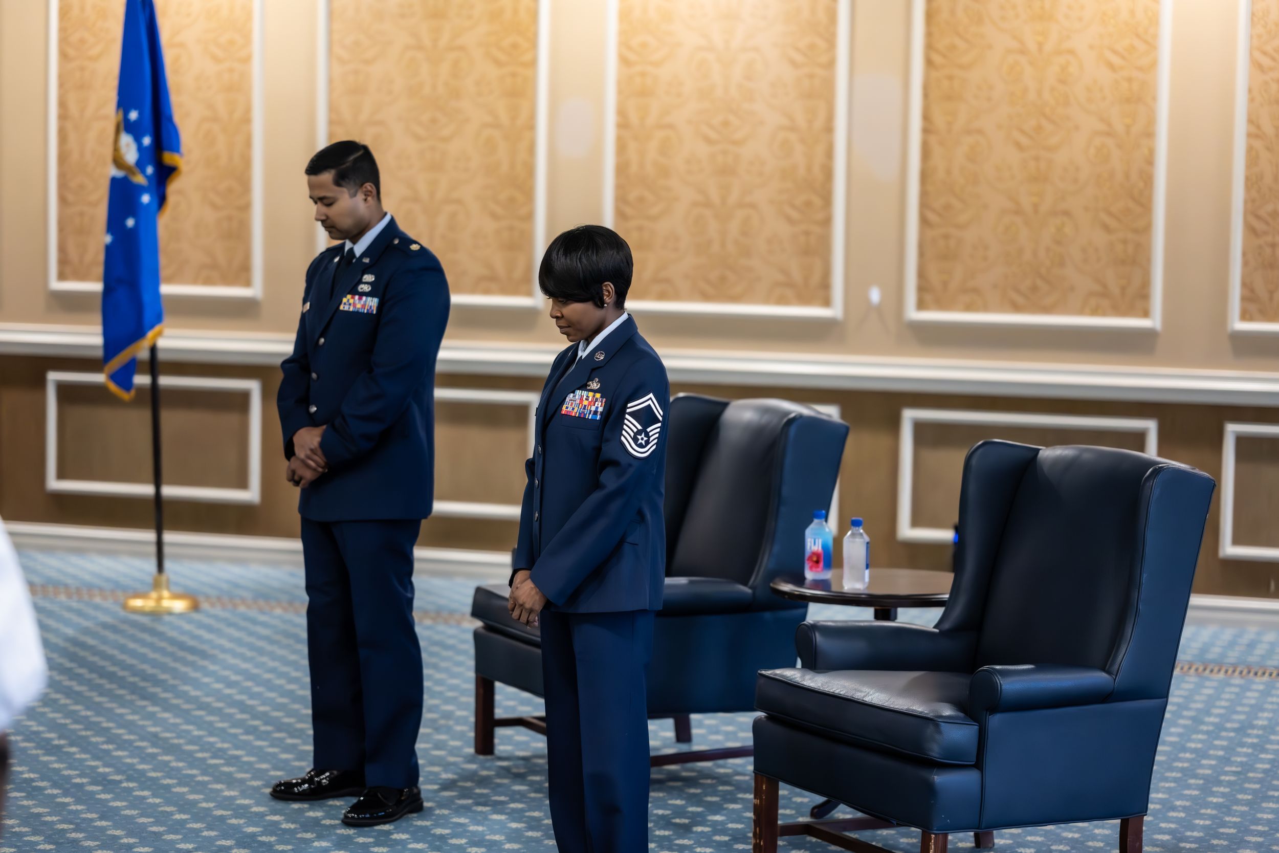 Service members stand at attention during a formal military ceremony in a conference room.