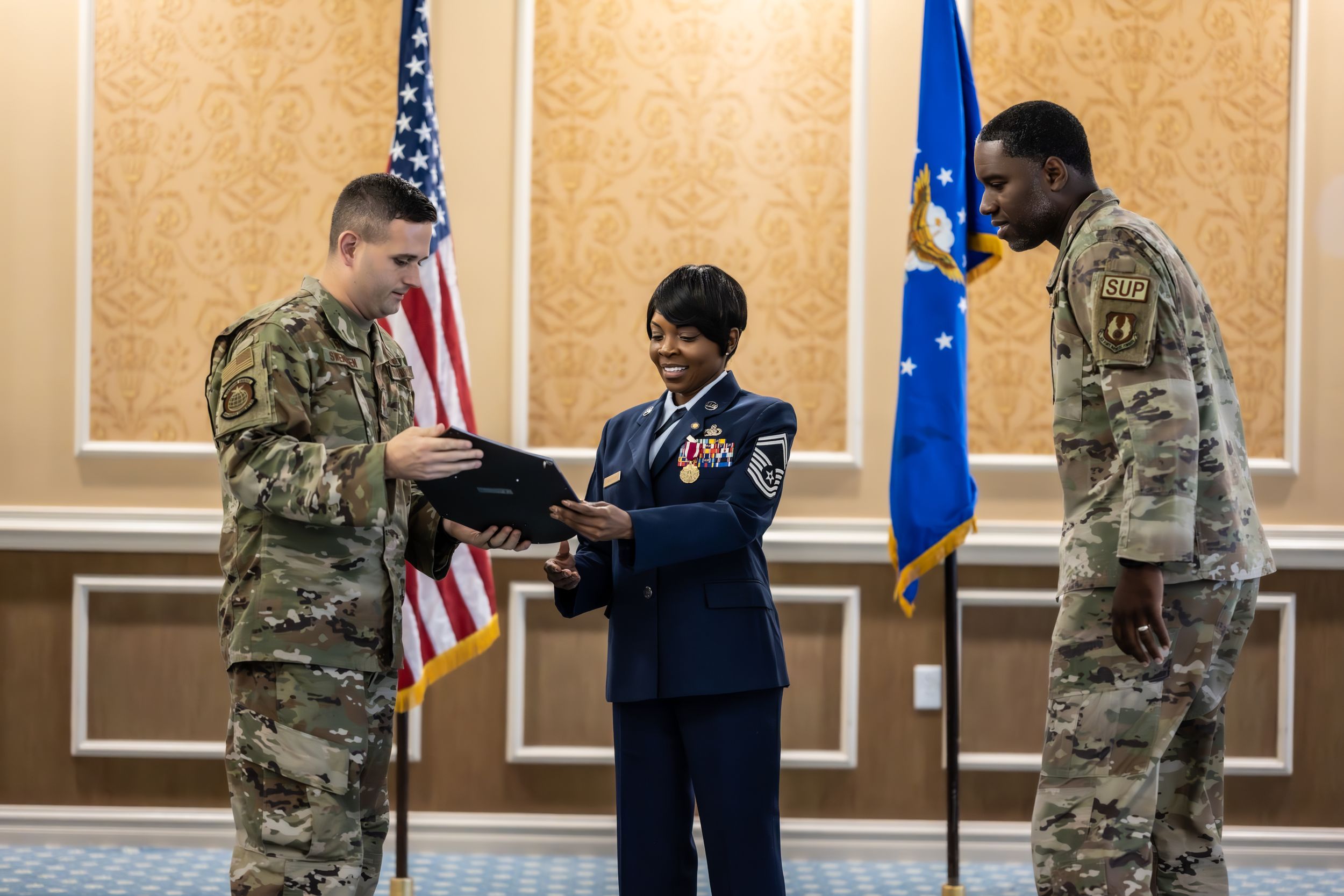 Military personnel gather for a formal ceremony with American and service flags on display.
