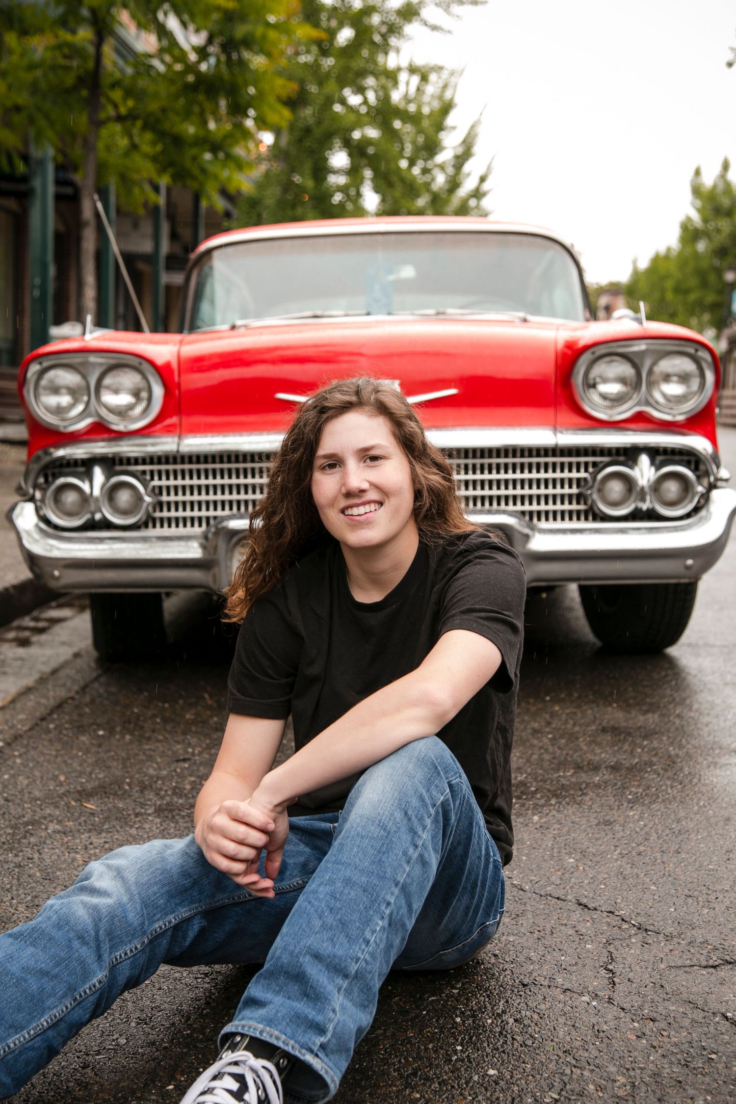 senior sitting in front of a red classic car