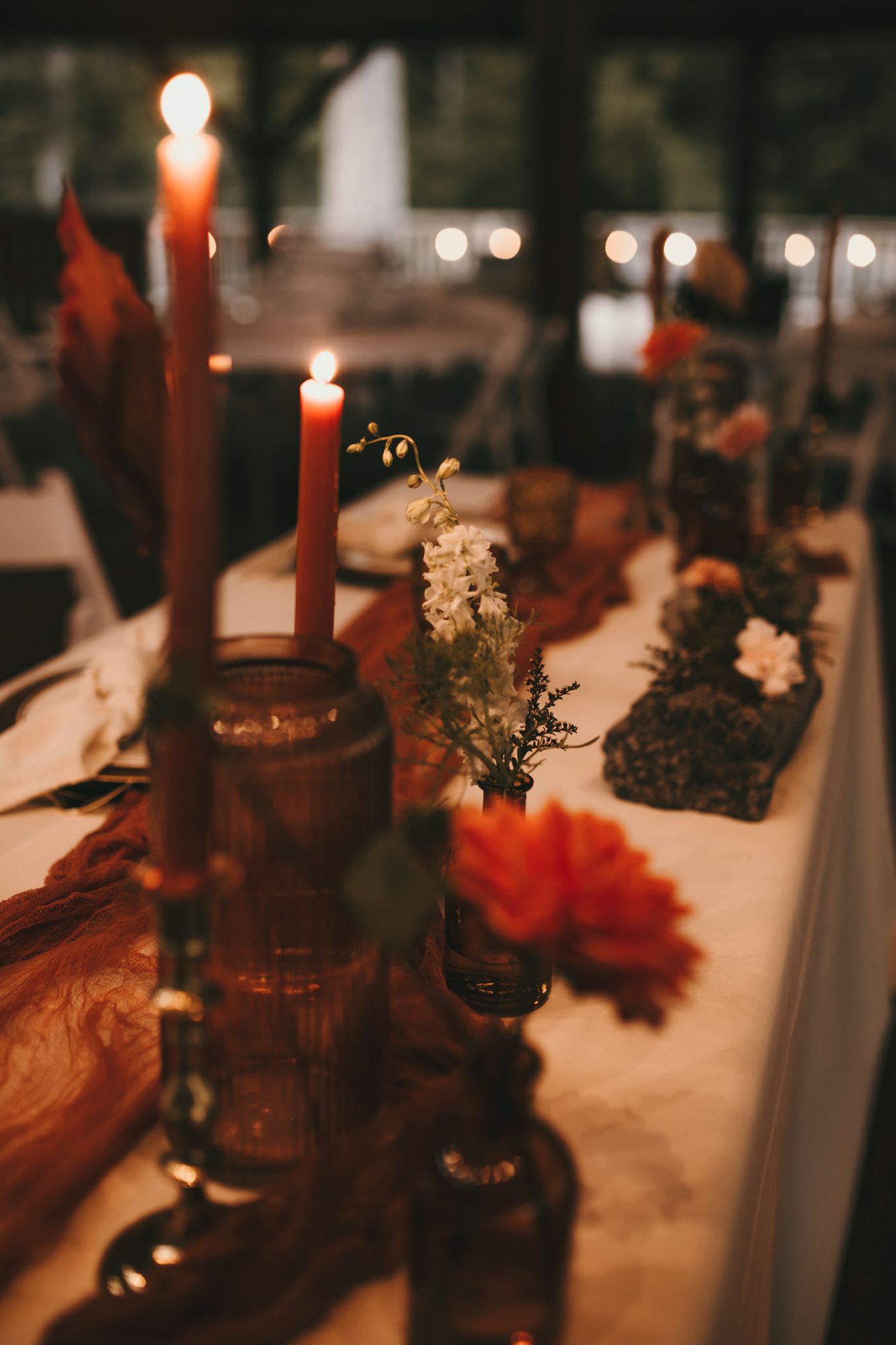 Moody wedding table setting with red candles and flowers in vintage glass bottles.