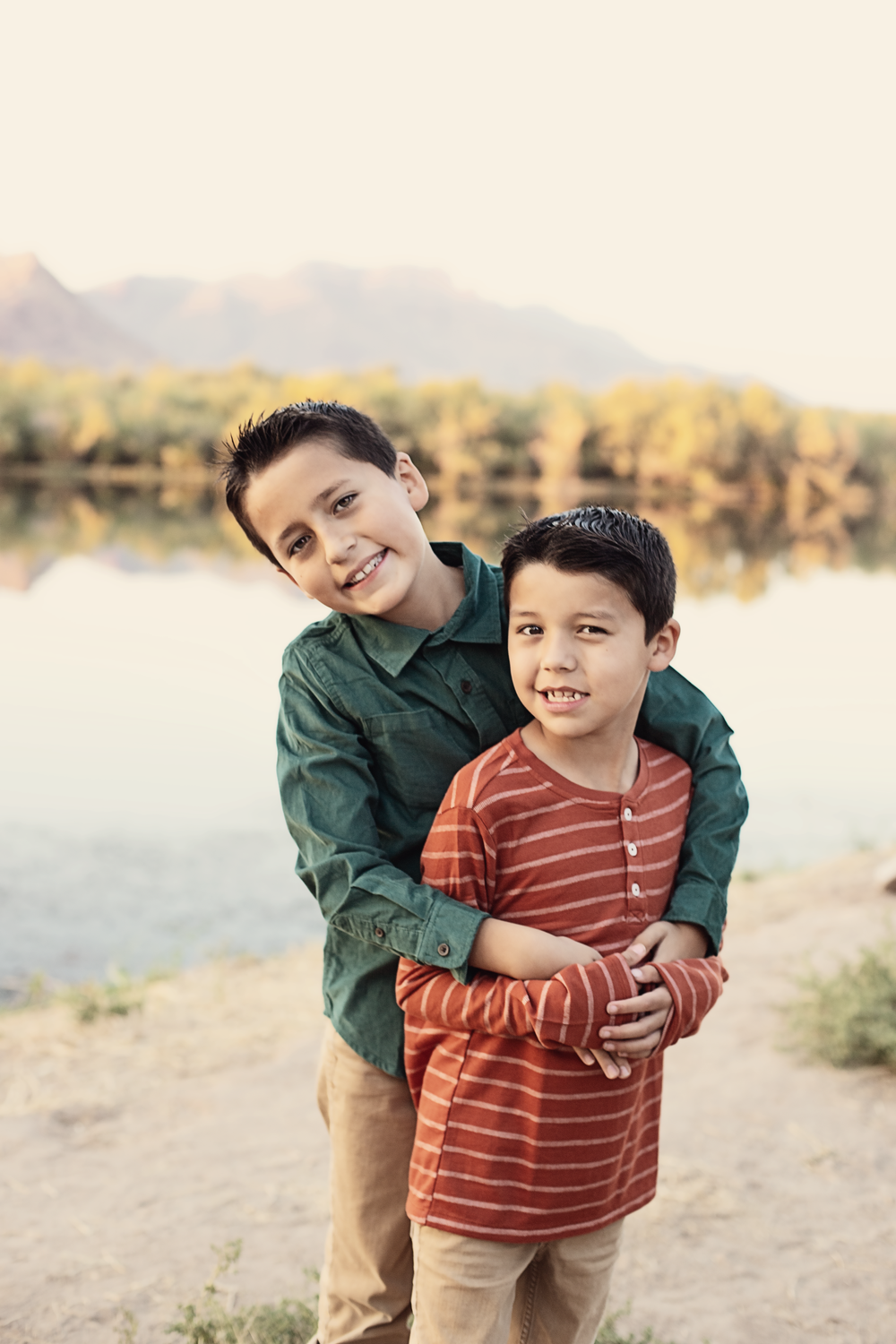 Candid family moments captured by lake with mountains in background during golden hour.