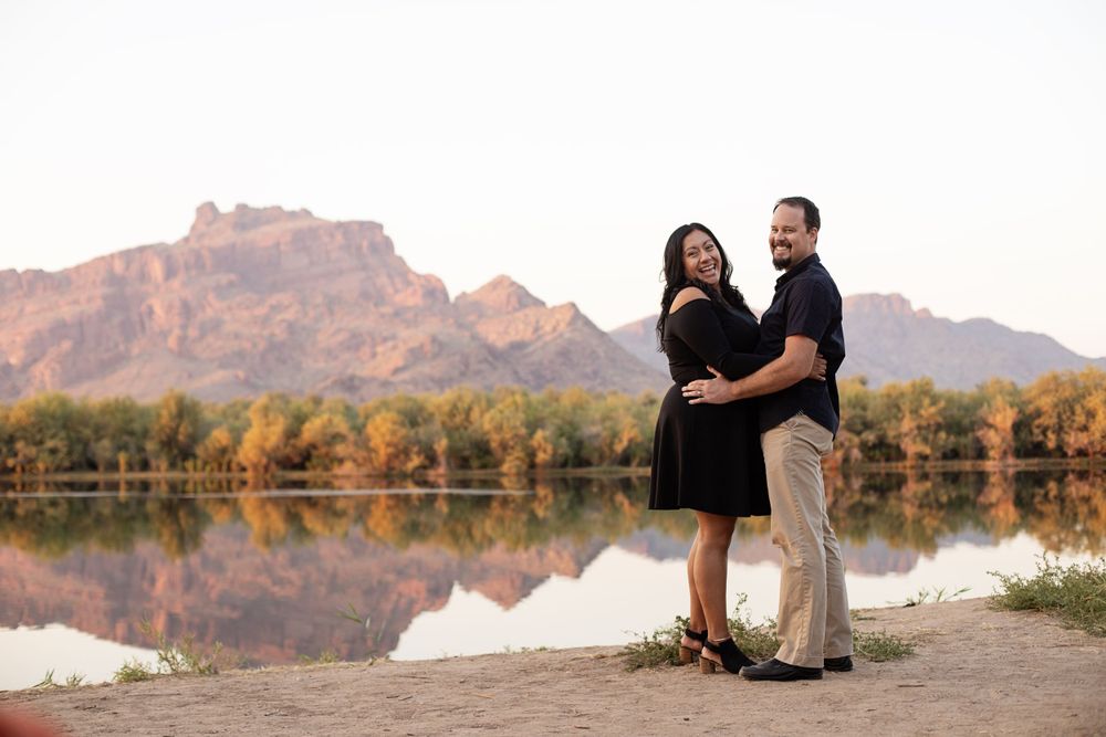 A family poses together against a scenic desert mountain backdrop with autumn trees and water reflections.