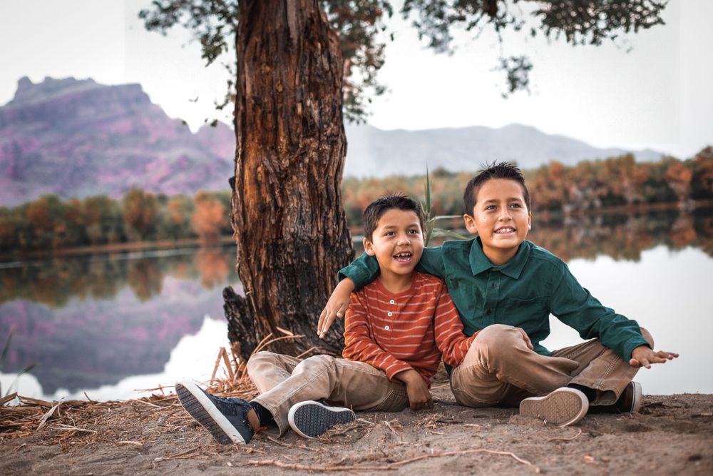 Siblings relaxing together under pine tree during lakeside photo session.