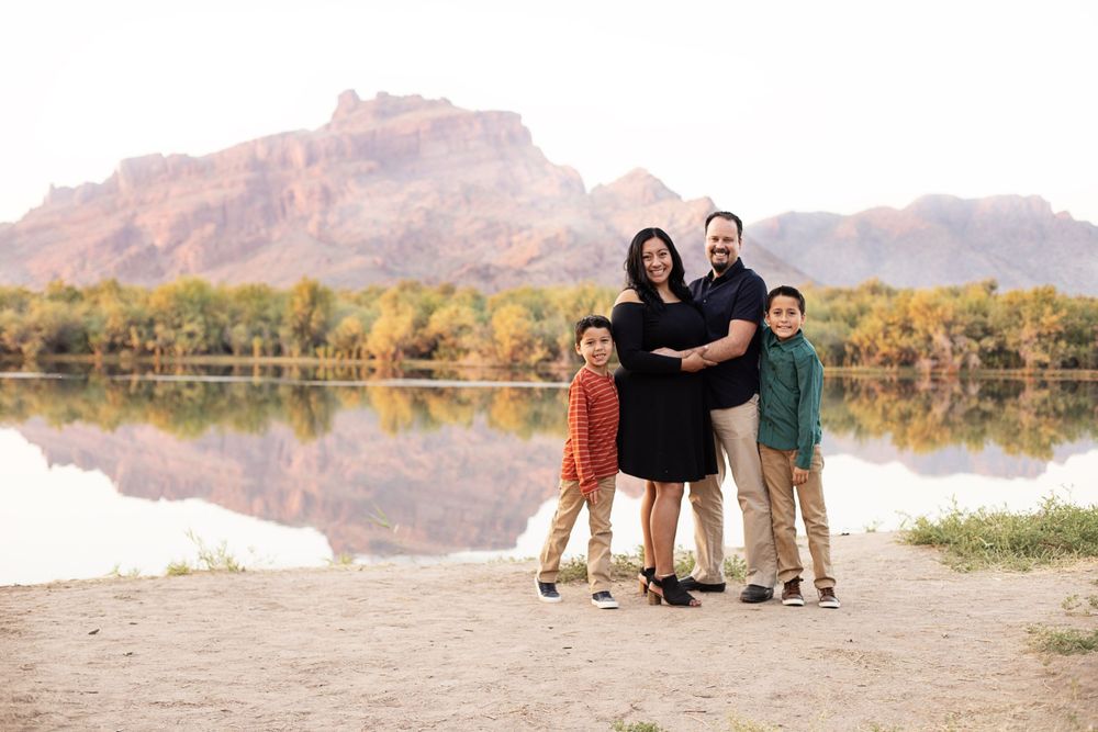 Family members sit together on rocks near a desert lake with mountains in the background during sunset.