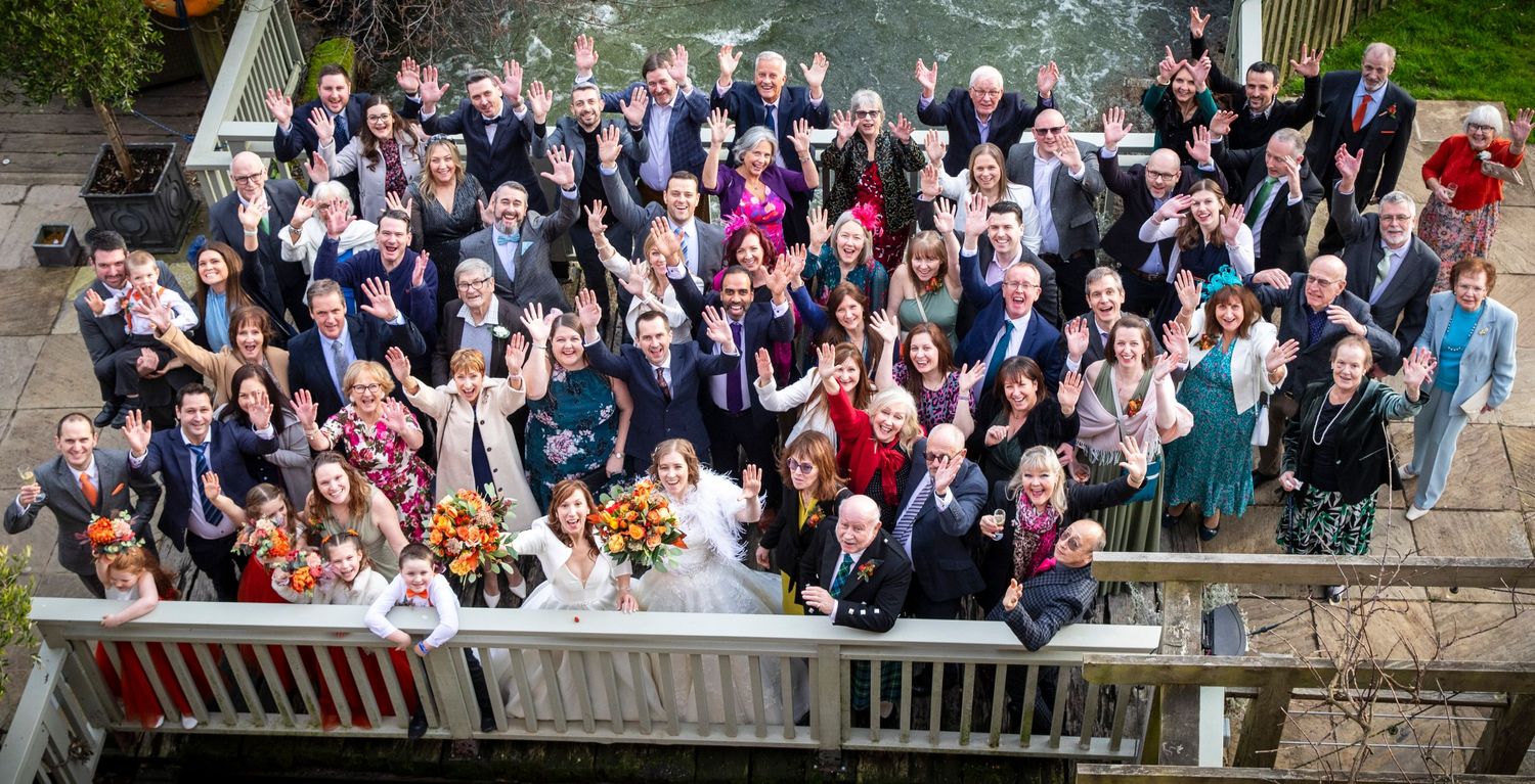 Large group wedding photo with guests gathered on outdoor terrace.