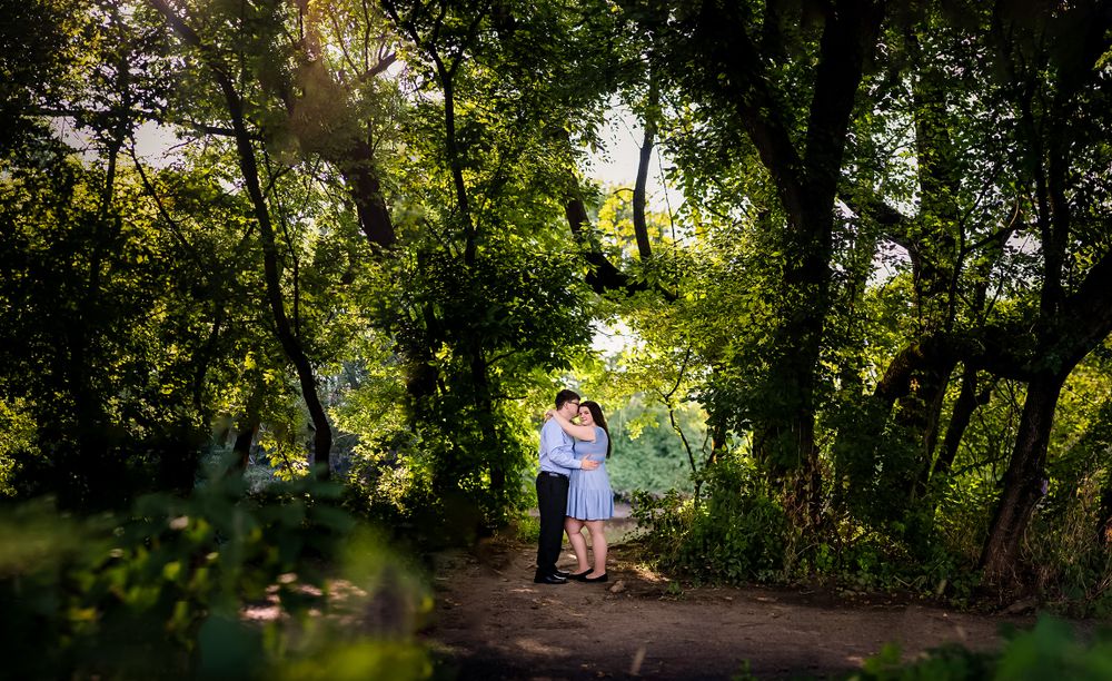 Sunlight streams through trees as a couple shares a moment on a wooded path.