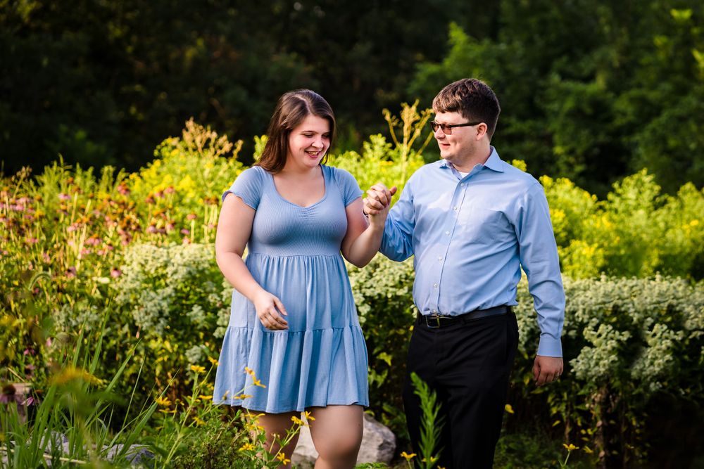 A couple walks together through a garden filled with yellow wildflowers on a sunny afternoon.