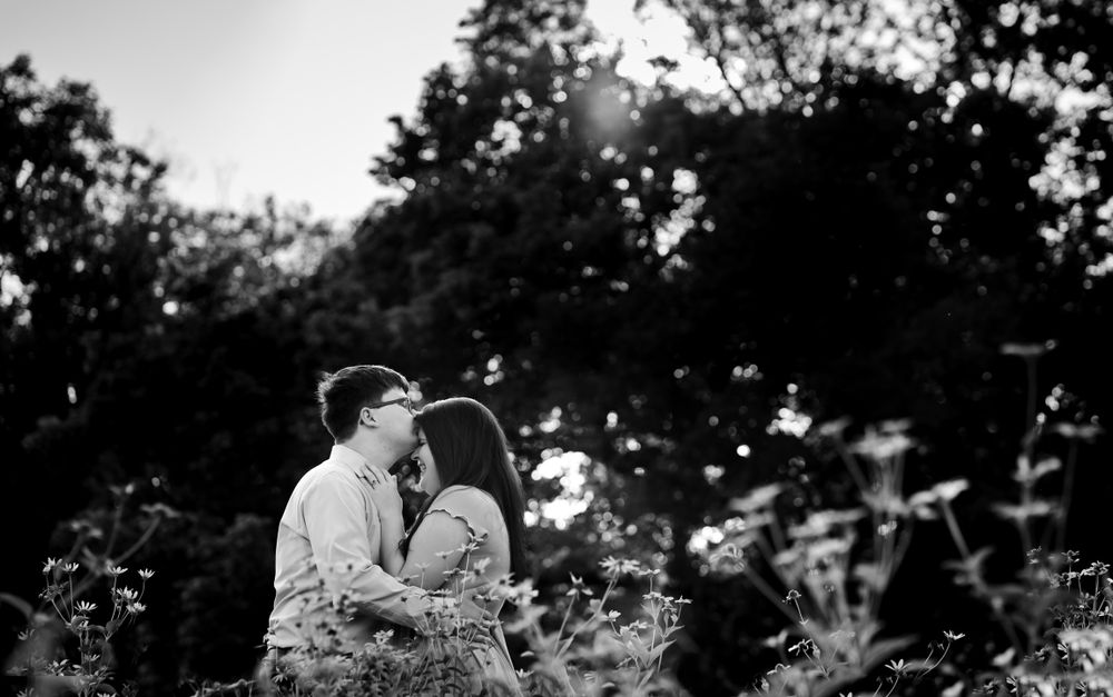 A romantic black and white portrait of a couple embracing among flowering plants.
