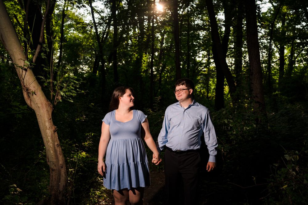 A couple laughs together while walking through a sunlit forest.