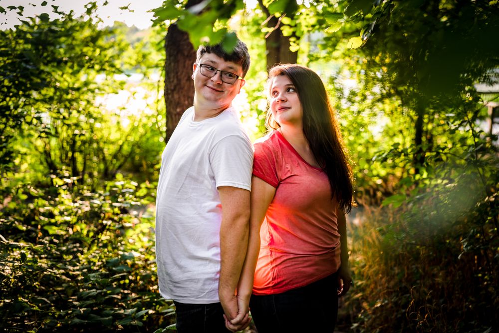 A couple poses together on a sunlit forest path during a summer photo session.