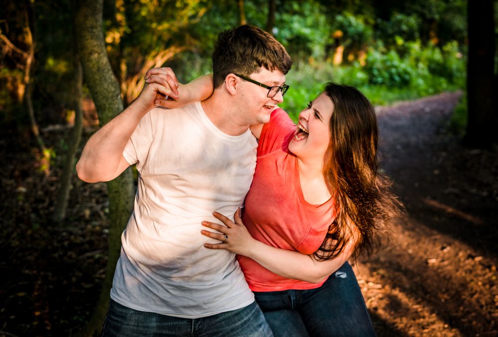 A couple shares a joyful moment while dancing together on a forest trail.