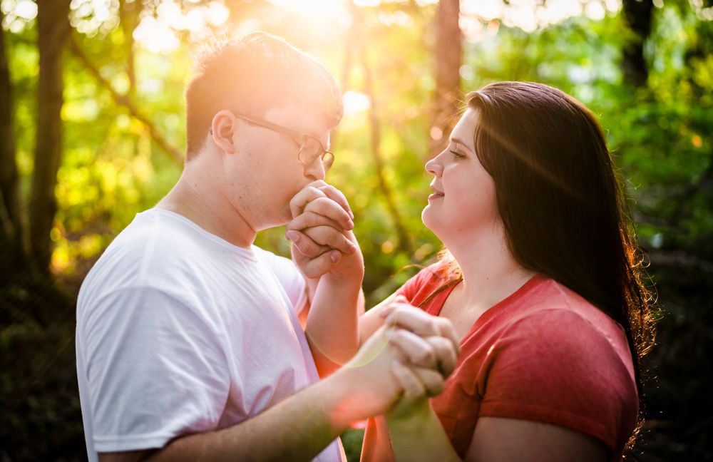 A couple laughs together in golden sunset light filtering through forest trees.