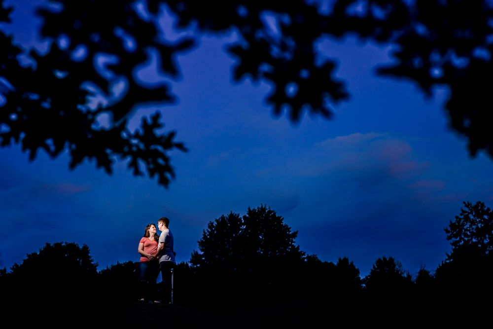 Couple's silhouette against deep blue twilight sky with tree branches overhead.
