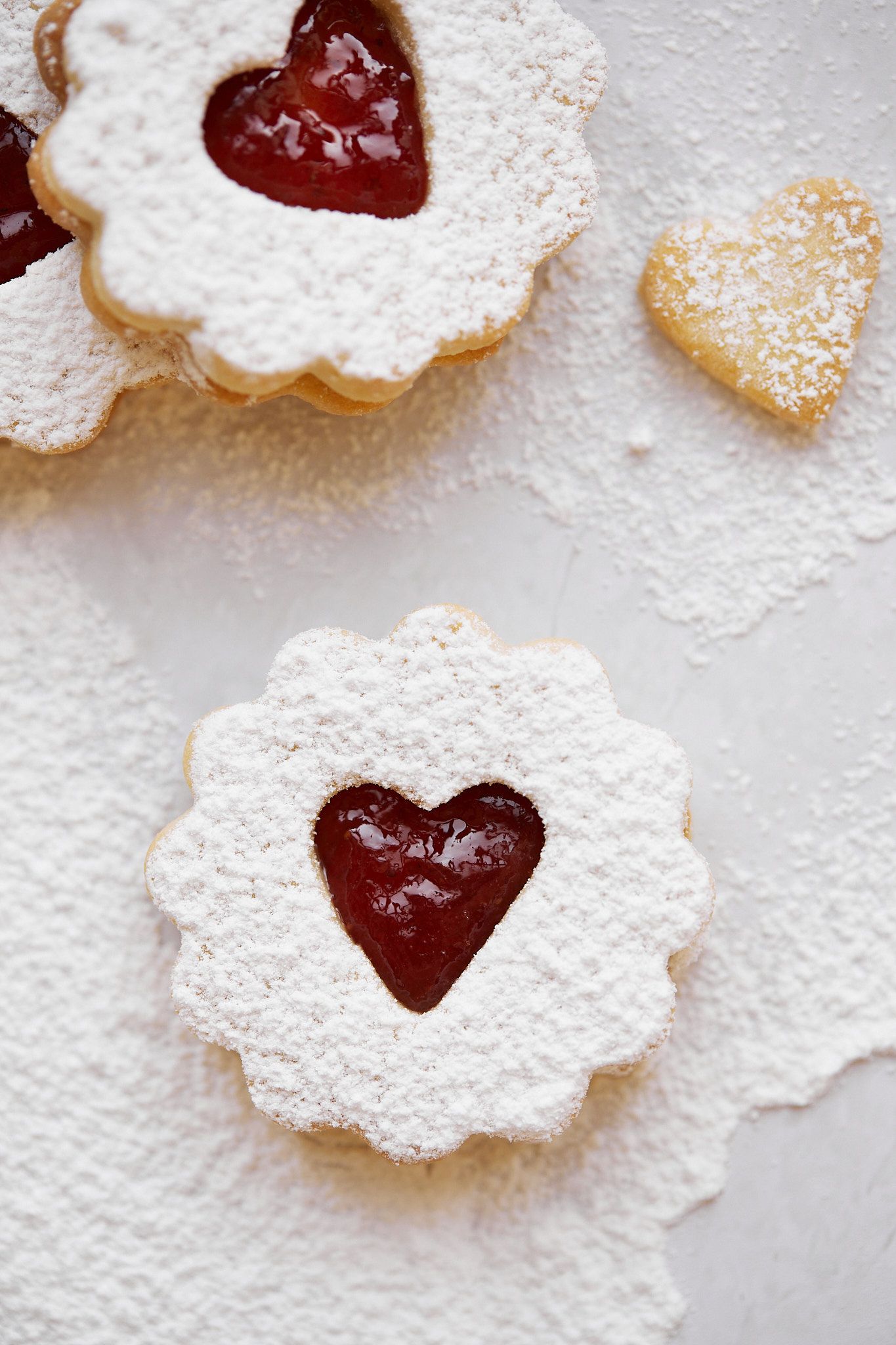 Heart-shaped Linzer cookies dusted with powdered sugar and filled with red raspberry jam.