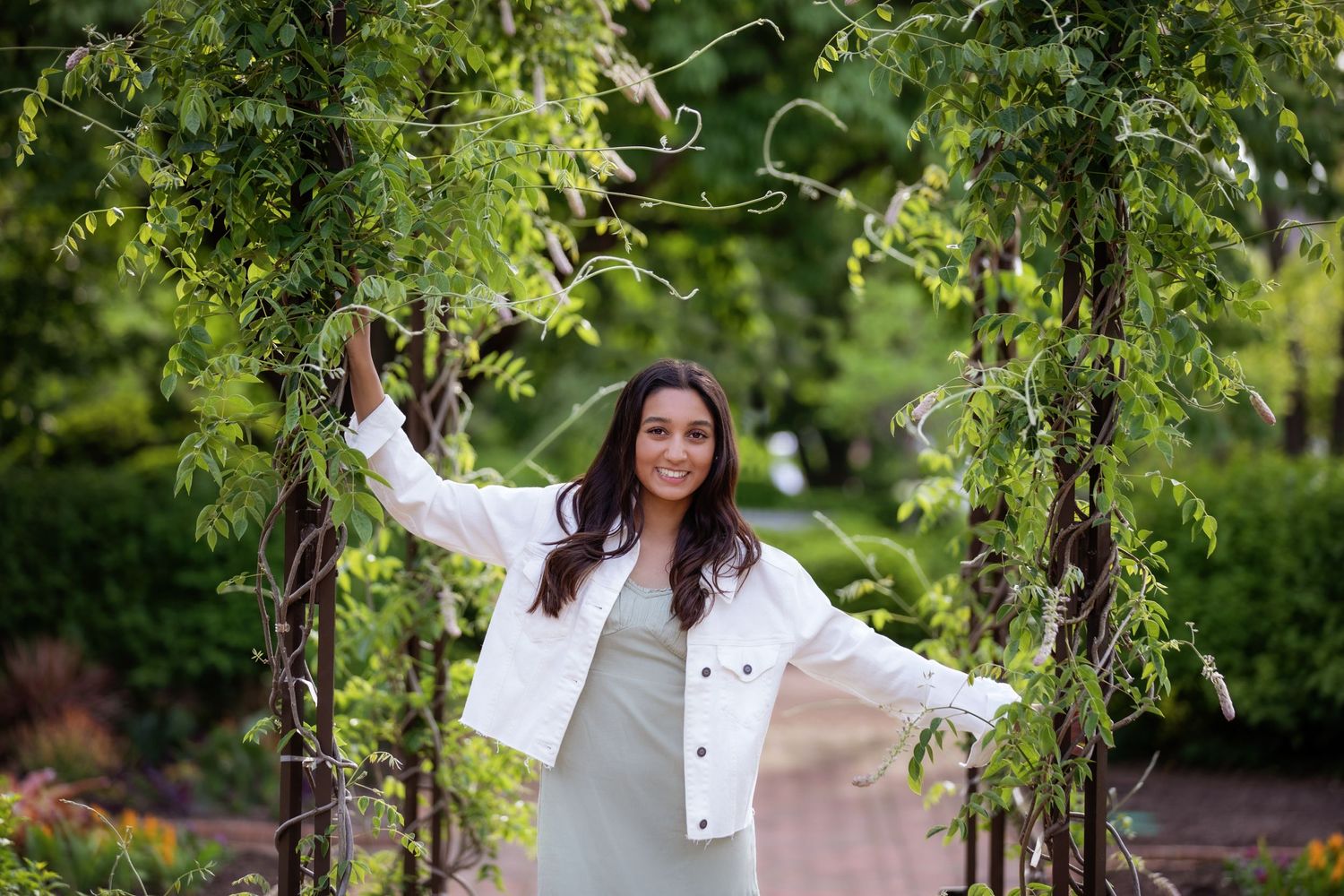 A white denim jacket and gray dress create an elegant outdoor portrait in a lush garden setting.