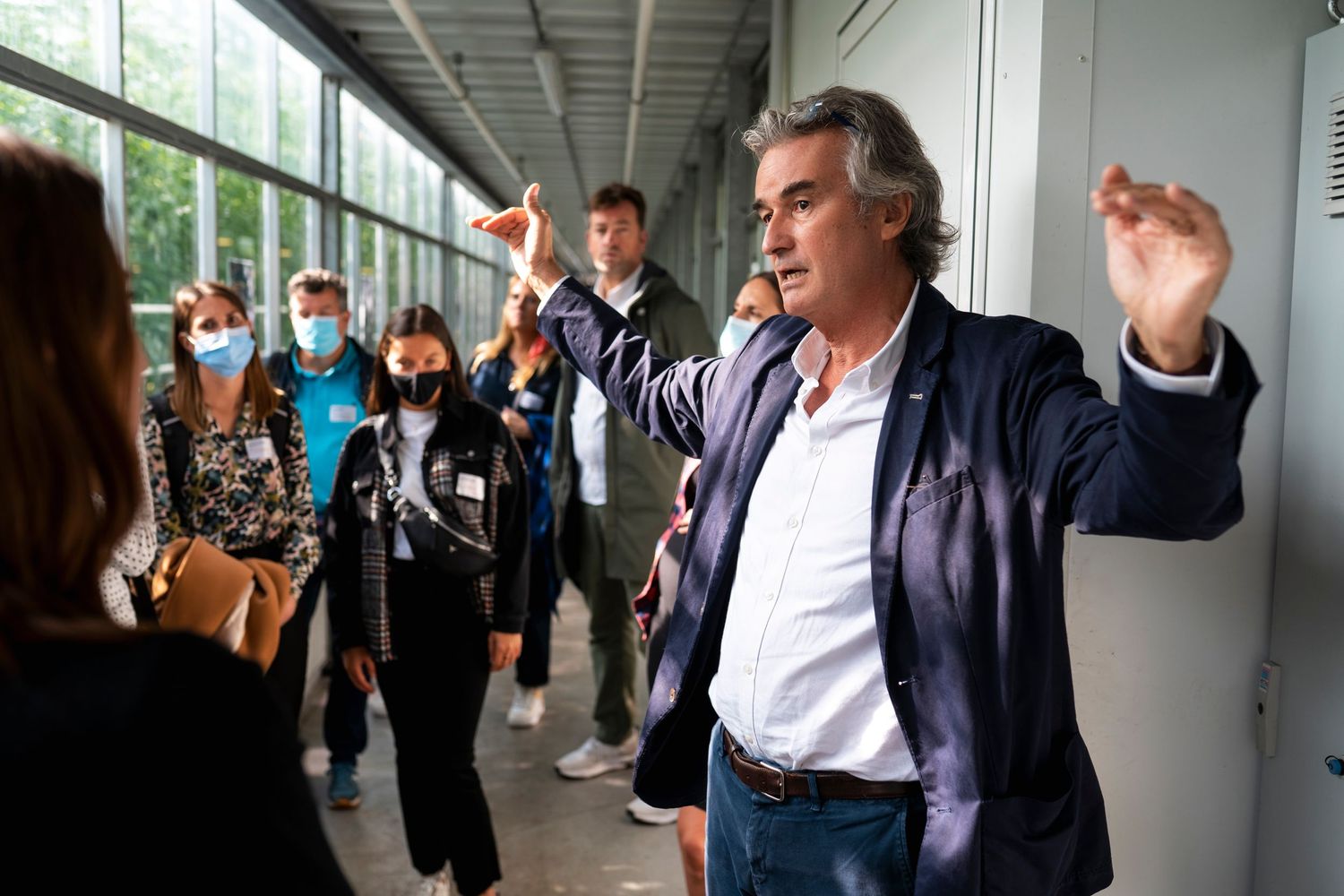 Animated speaker gesturing to masked audience in a hallway during presentation.