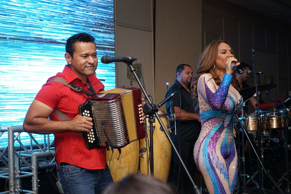 Musicians perform on stage with accordion and vocals at a colorful indoor concert.