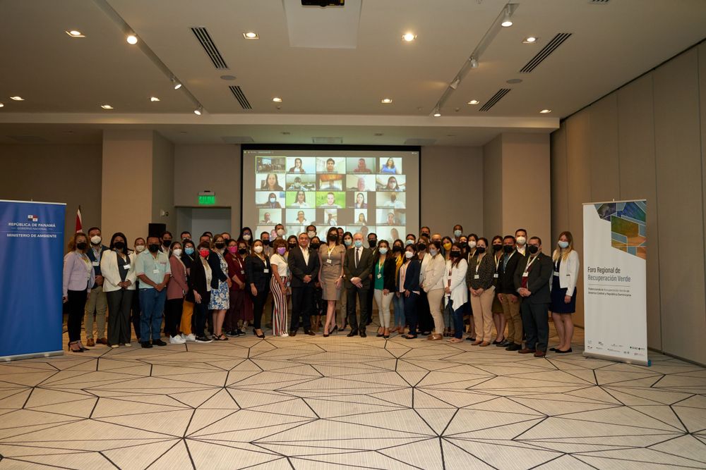 Large group photo of professional conference attendees in formal attire with projection screen.