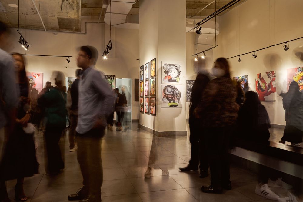 People viewing artwork in a dimly lit modern art gallery with framed pieces on walls.