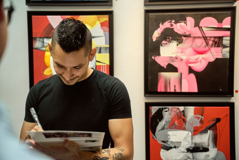 Person in black t-shirt looking at artwork in gallery with colorful abstract paintings.