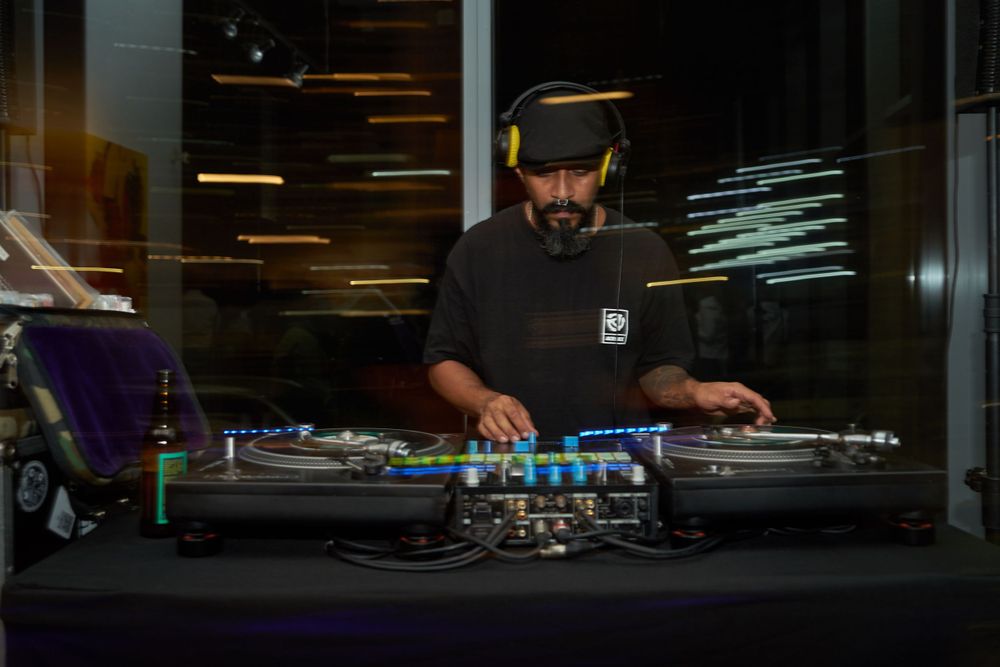 DJ performing at a mixing console in dark venue with equipment and lighting.
