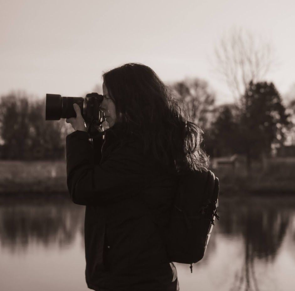 Silhouette of photographer with camera against lake at dusk.
