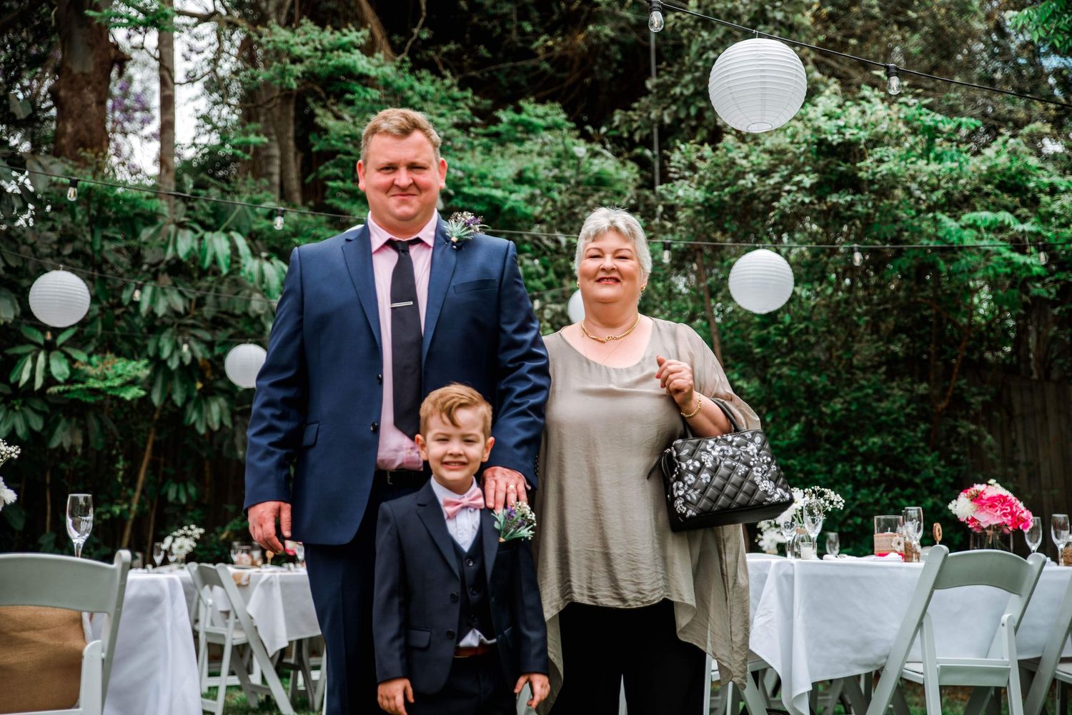 A family poses together under white paper lanterns at a backyard wedding reception.